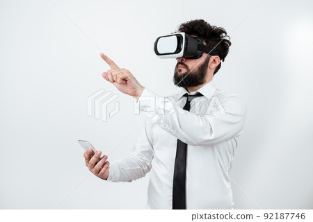 Man Holding Mobile Phone, Wearing Vr Glasses And Pointing On Recent Updates With One Finger. Businessman Having Virtual Reality Eyeglasses, Cellphone And Presenting New Idea. Man Holding Mobile Phone, Wearing Vr Glasses And Pointing On Recent Updates With One Finger. Businessman Having Virtual Reality Eyeglasses, Cellphone And Presenting New Idea. 92187746