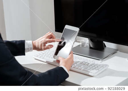 Businesswoman Holding Mobile Phone With Important Announcements Sitting On Desk With Computer. Woman In Suit Having Cellphone With Crutial Informations. 92188029