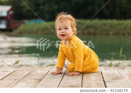 Cute Caucasian smiling child sitting on the pier by the river. Outdoors. The concept of a happy childhood and childhood autism 92188270