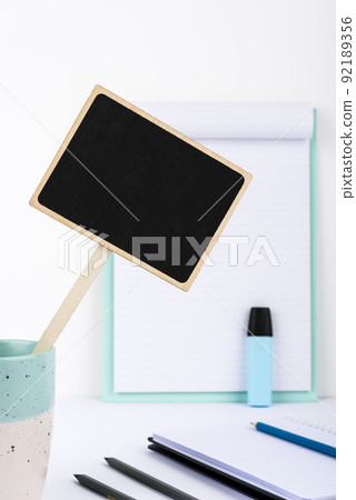 Small Blackboard With Important Message In Cup On Desk With Clipboard, Notebooks And Marker. Little Board With Crutial Information On Table With Paper. Current Ideas Presented Small Blackboard With Important Message In Cup On Desk With Clipboard, Notebooks And Marker. Little Board With Crutial Information On Table With Paper. Current Ideas Presented 92189356