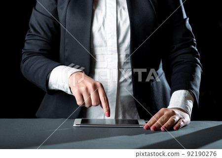 Businesswoman Having Tablet On Desk And Pointing On It With One Finger. Woman With Phone Showing Recent Updates. Executive Displaying Important News. Businesswoman Having Tablet On Desk And Pointing On It With One Finger. Woman With Phone Showing Recent Updates. Executive Displaying Important News. 92190276