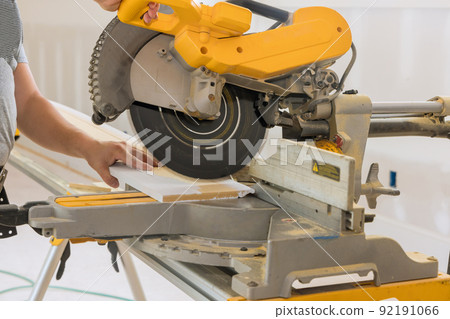 Construction worker cuts wood moldings baseboard on the miter saw 92191066