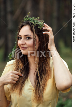 Beautiful woman in wreath of herbs and flowers in forest on sunny day. Portrait of candid woman 92195126