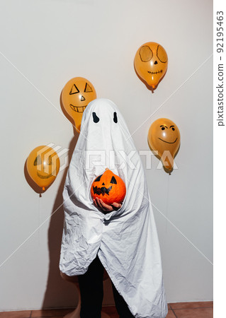 Happy Halloween. Ghost is holding orange pumpkin in hand. Child in white suit, painted yellow balloons. Different emotions of joy, anger, laughter. Festive design, party concept. Soft Selective focus 92195463
