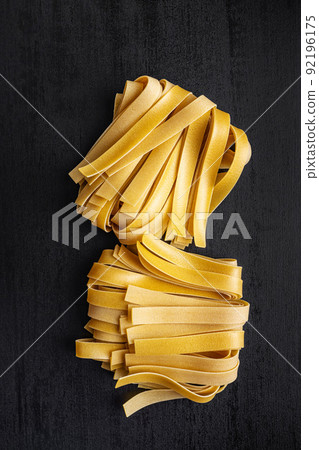 Uncooked pappardelle pasta on black table. Uncooked pappardelle pasta on black table. 92196175