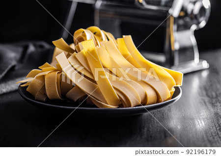 Uncooked pappardelle pasta on plate on black table. Uncooked pappardelle pasta on plate on black table. 92196179