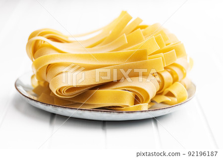Uncooked pappardelle pasta on plate on white table. 92196187