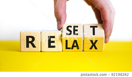 Relax and reset symbol. Businessman turns cubes and changes the word 'relax' to 'reset'. Beautiful yellow table, white background. Business, relax and reset concept. Copy space. 92198262