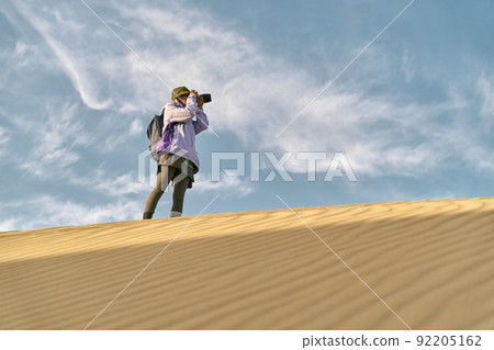 asian woman photographer taking a photo on top of a sand dune asian woman photographer taking a photo on top of a sand dune 92205162