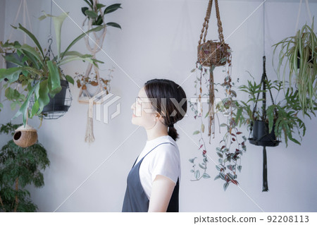 A Japanese woman in a dress looking somewhere in a room with bright plants 92208113