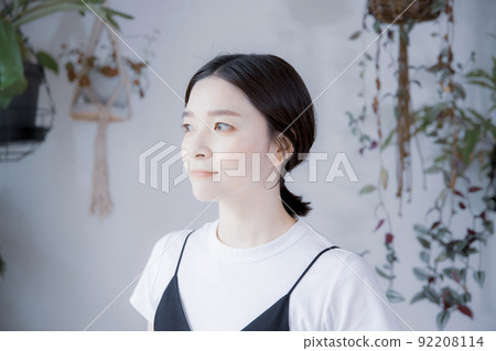 A Japanese woman in a dress looking somewhere in a room with bright plants 92208114