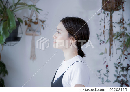 A Japanese woman in a dress looking somewhere in a room with bright plants A Japanese woman in a dress looking somewhere in a room with bright plants 92208115