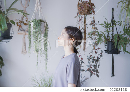 A Japanese woman in a dress looking somewhere in a room with bright plants A Japanese woman in a dress looking somewhere in a room with bright plants 92208118