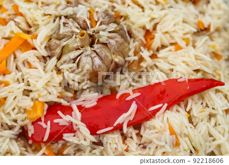 Cooking pilaf rice in a large cast iron pot over the fire. Garlic bulb and red hot pepper Cooking pilaf rice in a large cast iron pot over the fire. Garlic bulb and red hot pepper 92218606