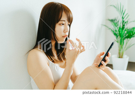 一位年輕女子一邊刷牙一邊看著她的智能手機 92218844