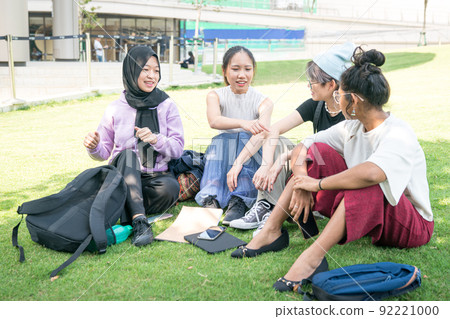 Group of young Asian women sitting on green lawn and chatting. 92221000