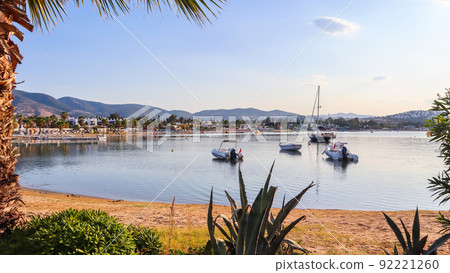 Beautiful bay with calm water, sandy beach, boats and yachts. Small town and green mountains on the coast of the Aegean sea 92221260