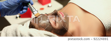 Spa centre worker applying clay mask on clients face with special tool Spa centre worker applying clay mask on clients face with special tool 92224891