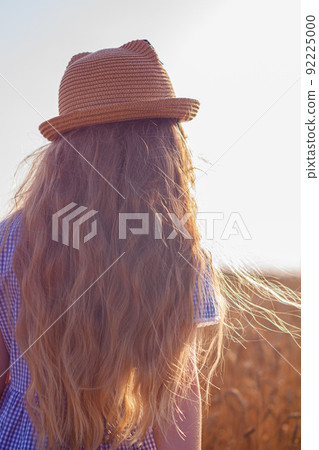 Adorable little girl in a straw hat, blue plaid summer dress in wheat field countryside.Child with long blonde wavy hair Adorable little girl in a straw hat, blue plaid summer dress in wheat field countryside.Child with long blonde wavy hair 92225000