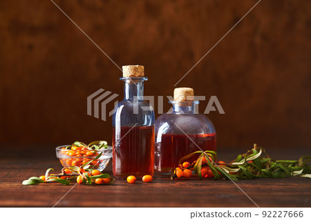 Glass bottle with sea buckthorn oil berries and sea buckthorn branches on wooden background Glass bottle with sea buckthorn oil berries and sea buckthorn branches on wooden background 92227666