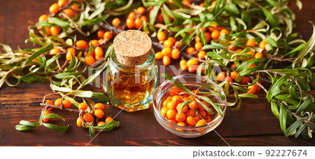 Glass bottle with sea buckthorn oil berries and sea buckthorn branches on wooden background Glass bottle with sea buckthorn oil berries and sea buckthorn branches on wooden background 92227674