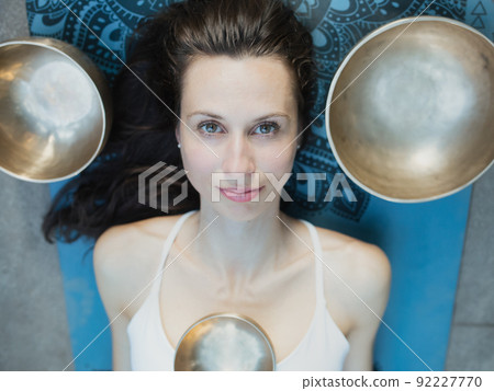 Yoga concept, meditation and sound therapy. Portrait of beautiful young caucasian woman surrounded by copper tibetan singing bowls and instruments 92227770