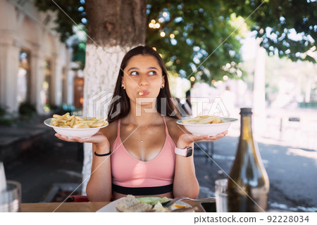 Young women hold french fries on white plates. Street cafe Young women hold french fries on white plates. Street cafe 92228034