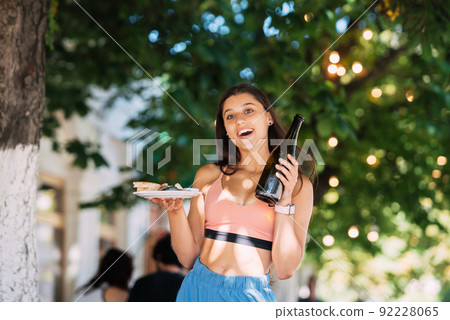 Young woman carries a plate of snacks and a drink in hands Young woman carries a plate of snacks and a drink in hands 92228065