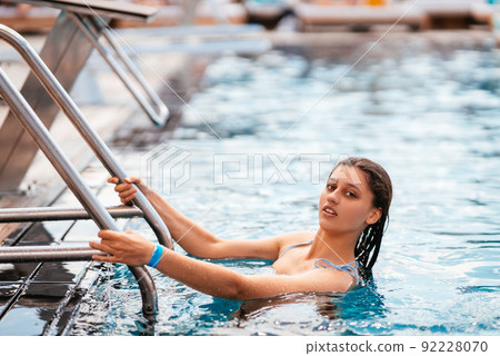 Young woman climbs the ladder out swimming pool 92228070
