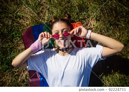 Young woman lying on LGBT flag in the park. Young woman lying on LGBT flag in the park. 92228731