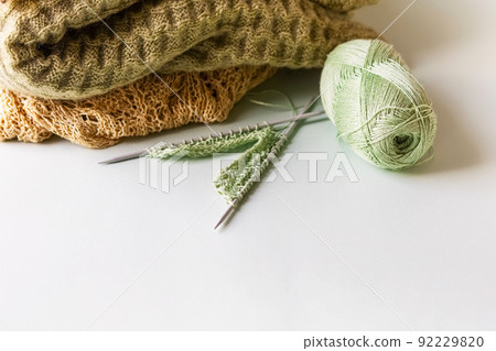 Green yarn thread with knitting needles and finished yarn products on a green background for knitting. 92229820