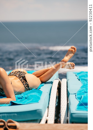 Young beautiful woman in swimsuit sunbathes on a sun lounger Young beautiful woman in swimsuit sunbathes on a sun lounger 92230411