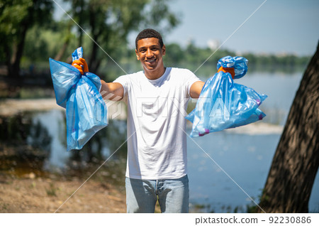 Smiling guy showing garbage bags at camera Smiling guy showing garbage bags at camera 92230886