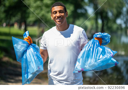 Guy holding trash bags smiling confidently at camera Guy holding trash bags smiling confidently at camera 92230896