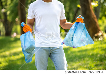 Man holding garbage bags in park without face Man holding garbage bags in park without face 92230931