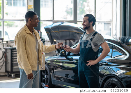 Man giving car key to auto repair worker Man giving car key to auto repair worker 92231089