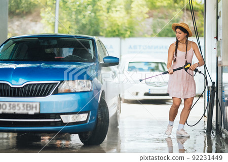 Brunette from a high-pressure hose washes the car 92231449