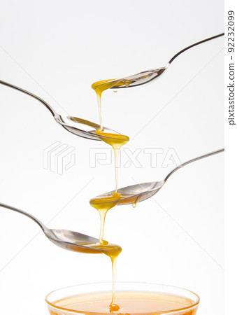 Fresh floral honey drips from a spoon into a spoon on a white background. Organic vitamin food. 92232099