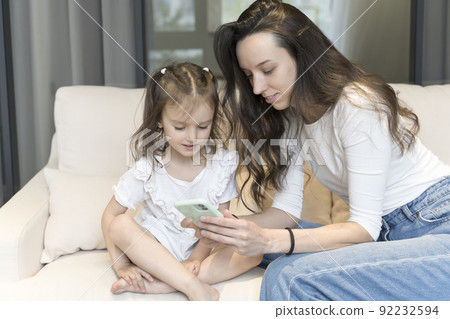 Mom and daughter use smartphone while playing and learning. Technology, internet and children. Parenthood, education, training, free time with children concept. 92232594