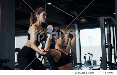 Sporty girl doing weight exercises with the help of her personal trainer at the gym. 92234660