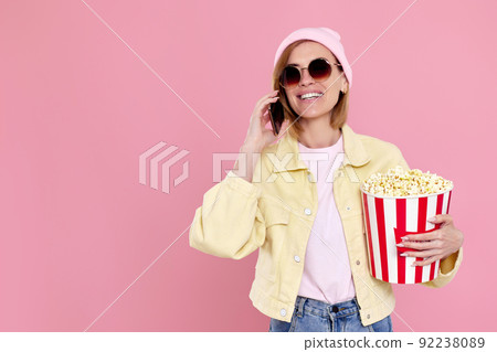 woman with bucket of popcorn talking on the phone woman with bucket of popcorn talking on the phone 92238089