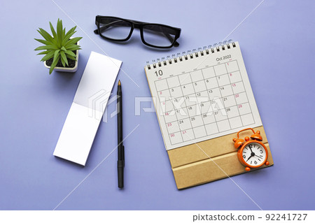 October 2022 desk calendar with alarm clock set at 8 o'clock on blue background. October 2022 desk calendar with alarm clock set at 8 o'clock on blue background. 92241727