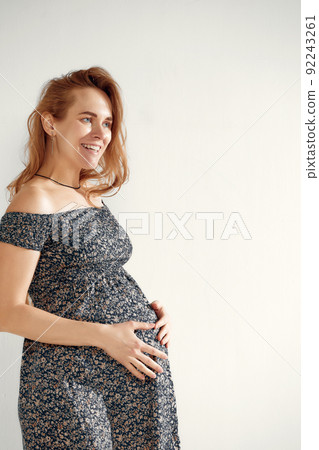 Pregnant woman over white background posing in studio. Beautiful pregnant woman with long hair in a summer dress on a white background 92243261