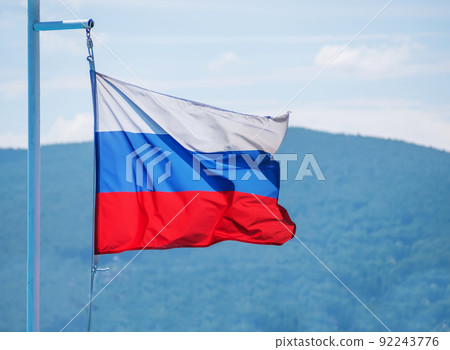 The Russian flag flutters against the blue sky and hills 92243776