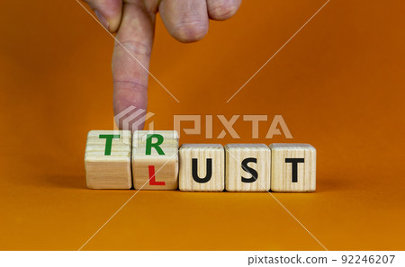 Lust or trust symbol. Businessman turns wooden cubes and changes the words 'lust' to 'trust'. Beautiful orange table, orange background. Business and lust or trust concept, copy space. 92246207