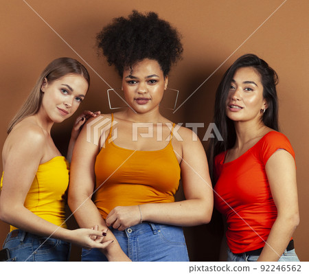 young pretty african and caucasian women posing cheerful together on brown background, lifestyle diverse nationality people concept close up 92246562