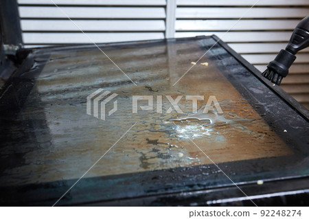 Experienced worker in rubber gloves steam-cleaning kitchen equipment. 92248274