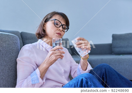 Mature sick woman taking pills with a glass of water Mature sick woman taking pills with a glass of water 92248690