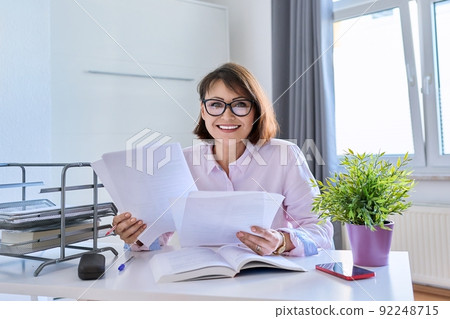 Middle-aged female working at home at a table with papers Middle-aged female working at home at a table with papers 92248715