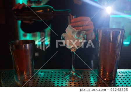 Barman in shirt and apron making an alcoholic drink with ice in a cocktail glass. Barman in shirt and apron making an alcoholic drink with ice in a cocktail glass. 92248868